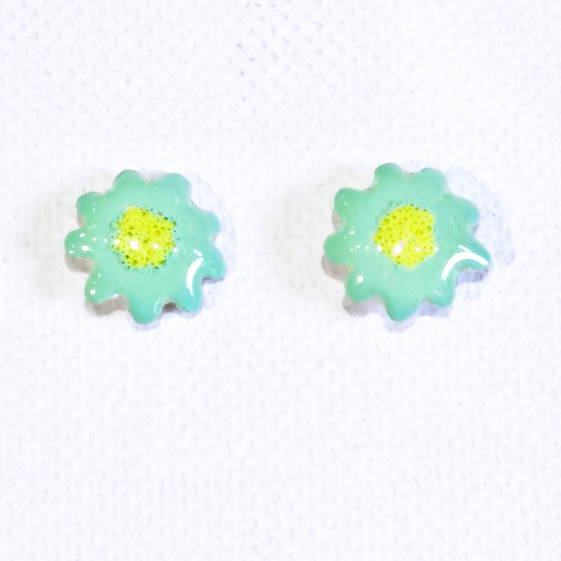 Light green silver stud earrings with yellow center .