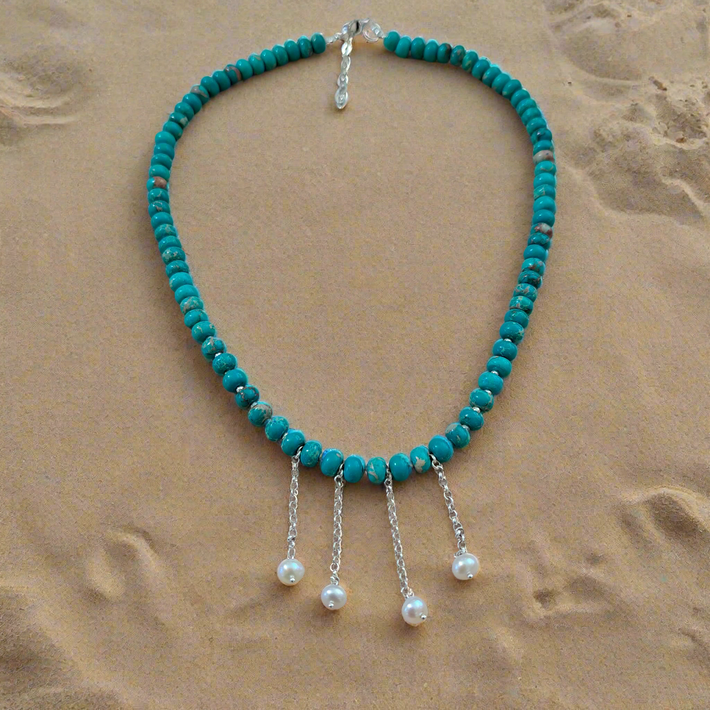 Turquoise beaded necklace with silver chains and pearls sitting at the sand
