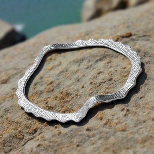 Silver textured Bracelet with wavy design sitting on a rock