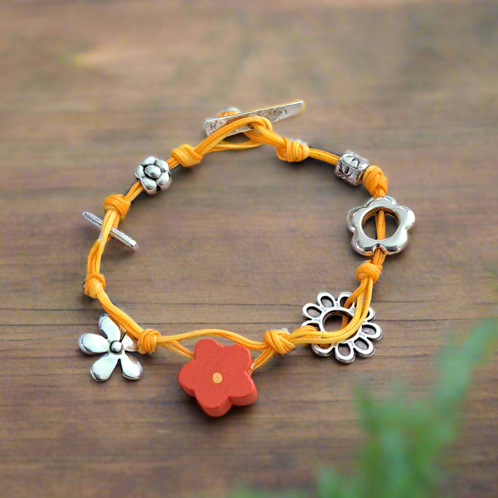 Bracelet with yellow cord, silver flower-shaped beads, and a red flower charm on a wooden surface.