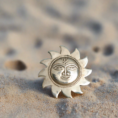 A sterling silver ring with an ethnic sun design set against a sandy background.