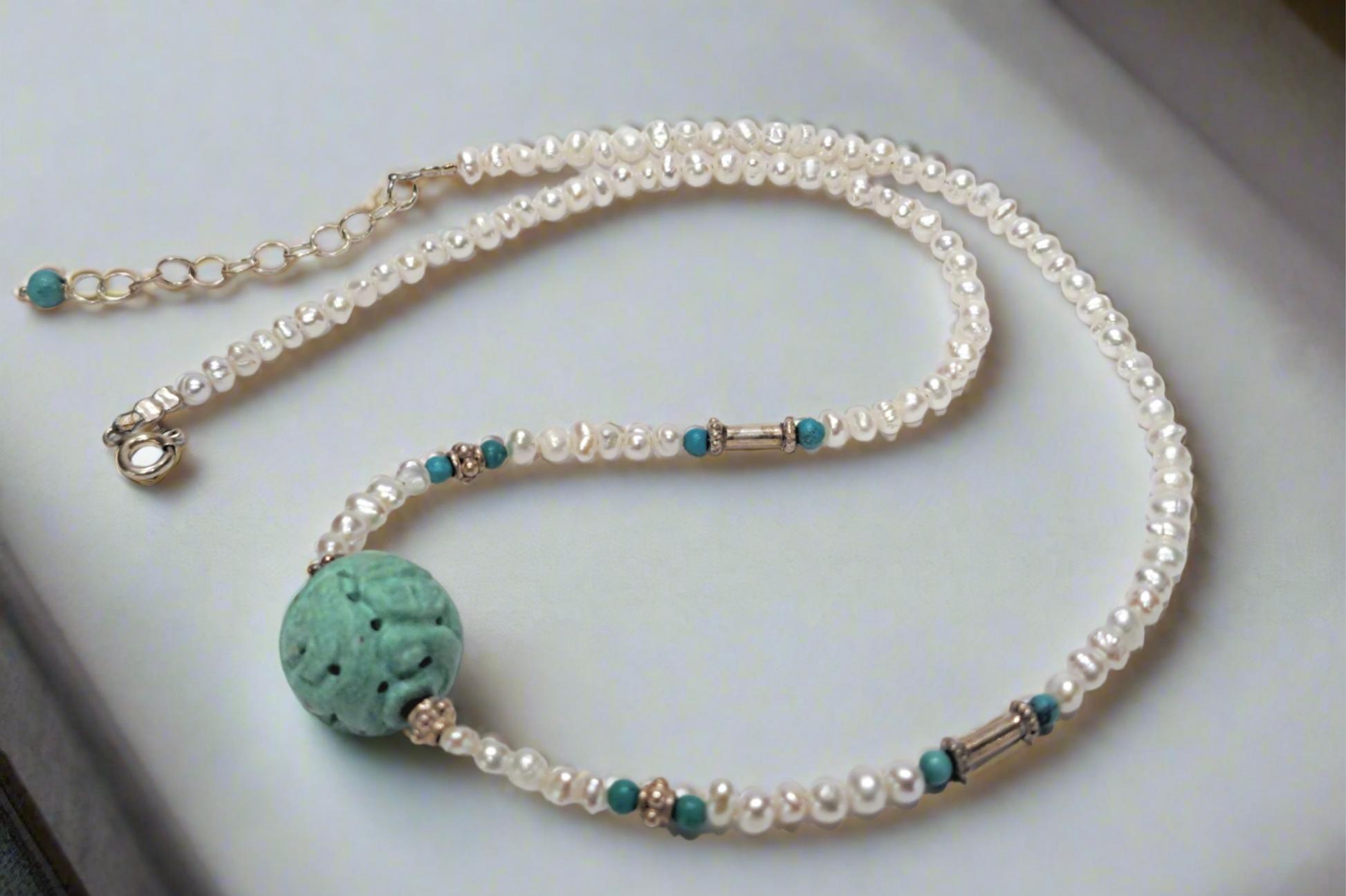 A handmade necklace featuring freshwater pearls, sterling silver accents, and a turquoise centerpiece.