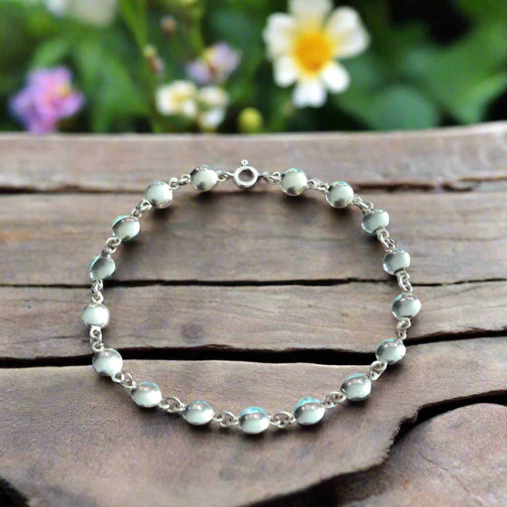 Silver bracelet with  flat round silver elements on a wooden surface with flowers in the background