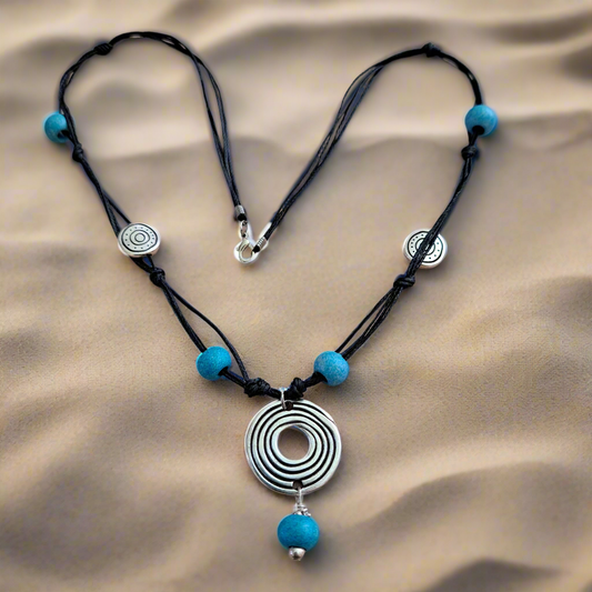 Necklace with black cord, blue beads, and silver spiral pendant  at the sand
