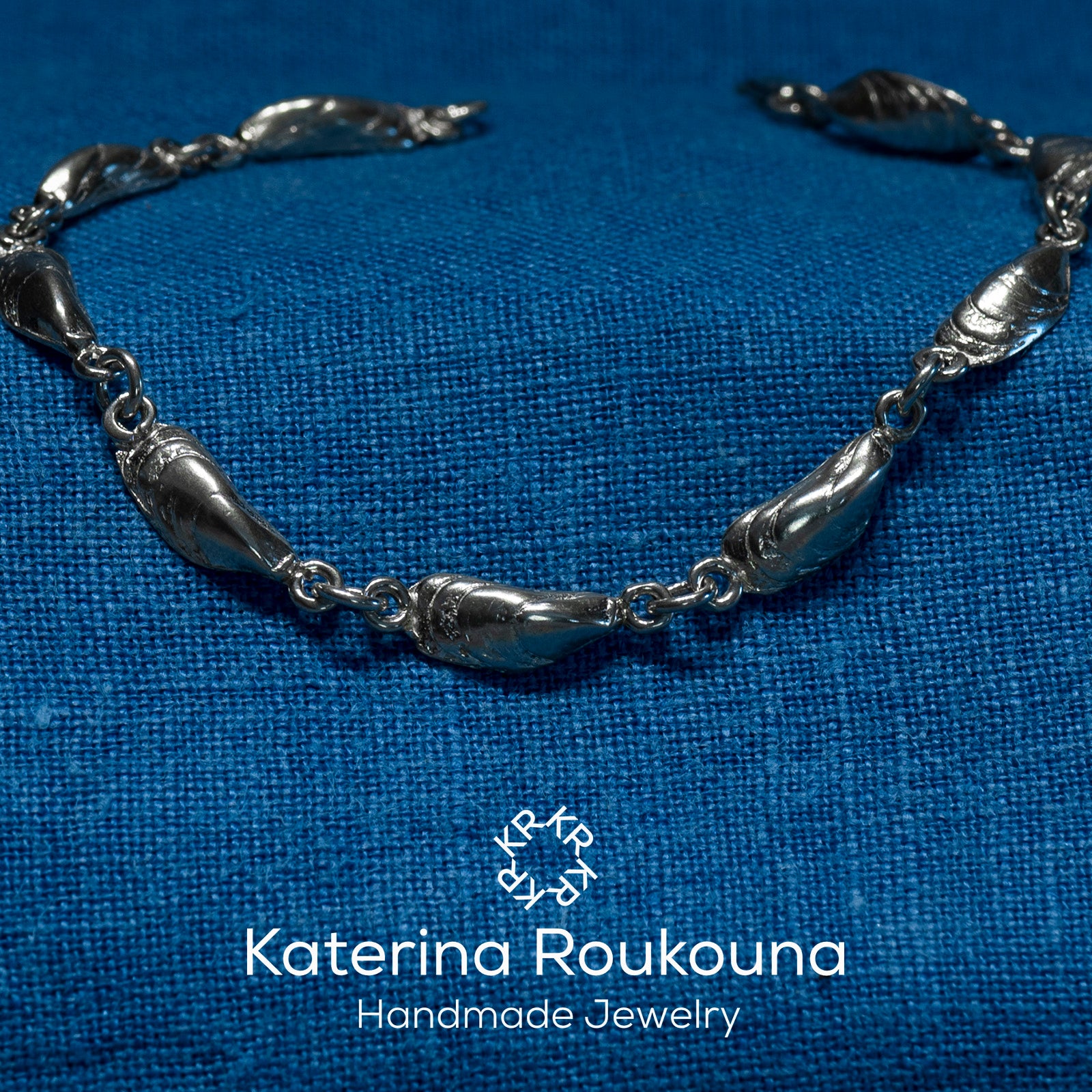 A sterling silver bracelet with intricate mussel-shaped details, displayed against a blue textured background.