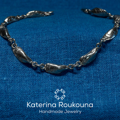 A sterling silver bracelet with intricate mussel-shaped details, displayed against a blue textured background.