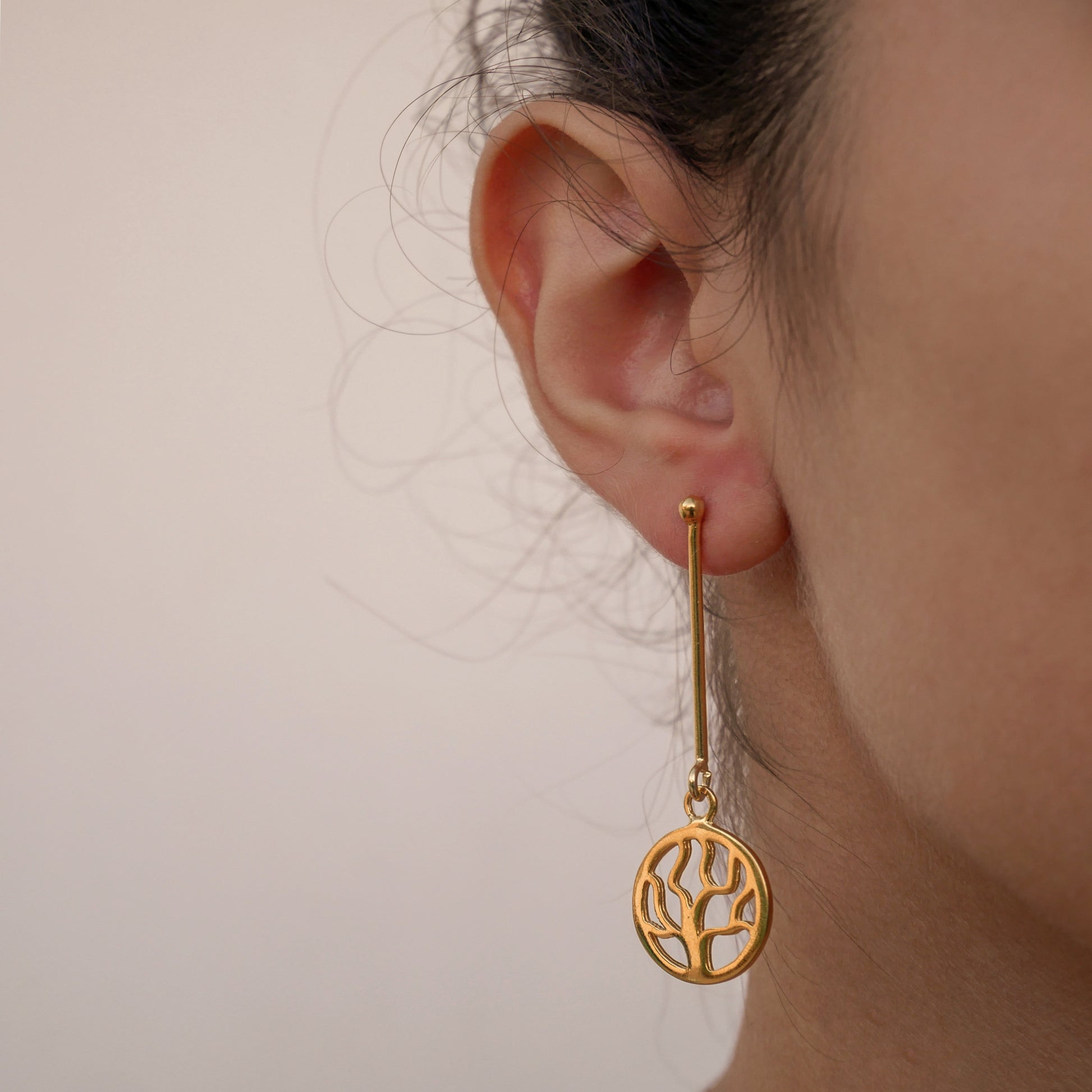 “Earrings made of  gold plated silver.They are constacted with a thick  vertikal wire and beneath the wire hangs a round design with the small round  tree without leaves and flowers. The design is perforated and elegant.”