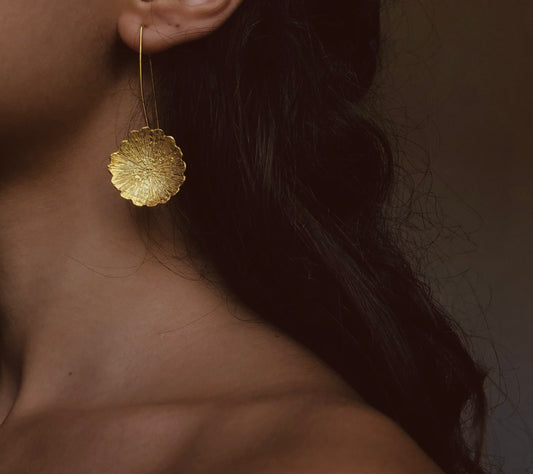 The picture shows a young woman wearing  gold plated long earring having masive flowers at the end of a long wire.